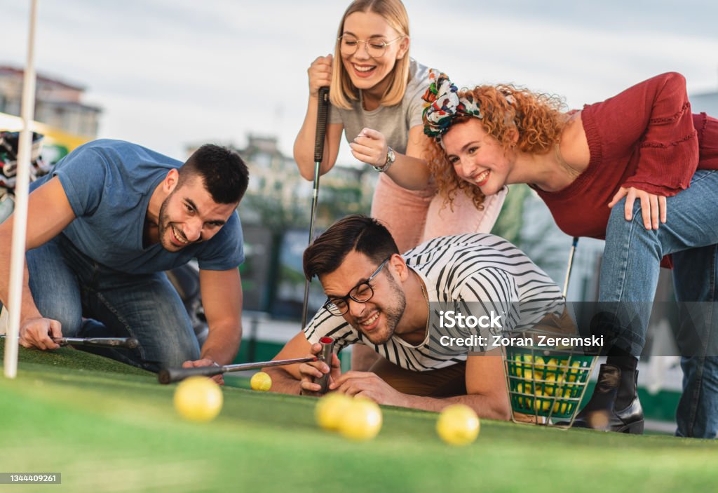 Group of smiling friends enjoying together playing mini golf in the city.